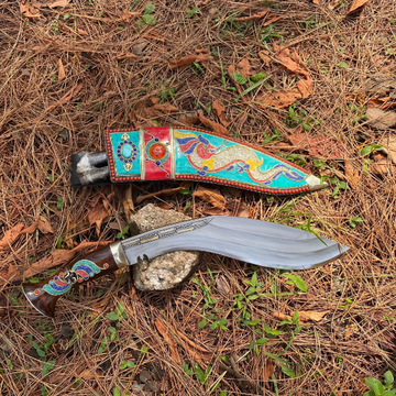 A 10 inch Farmer 3 Chirra Kukri knife with a hand-bitten Gurkha blade with decorative design in sheath, resting on a grass in a natural outdoor setting with trees in the background.